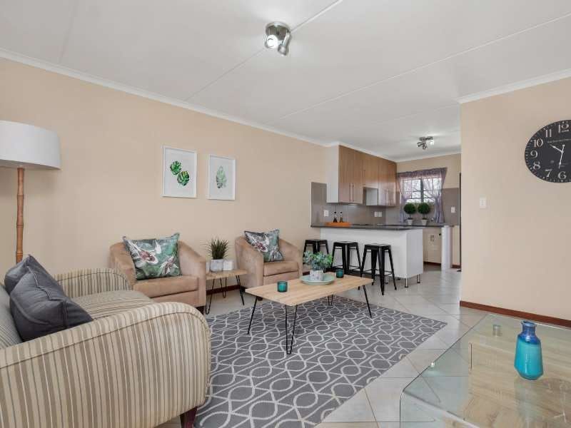 An open-plan living area featuring a modern kitchen with a breakfast island, tiled flooring, and neutral wall finishes throughout the space.
