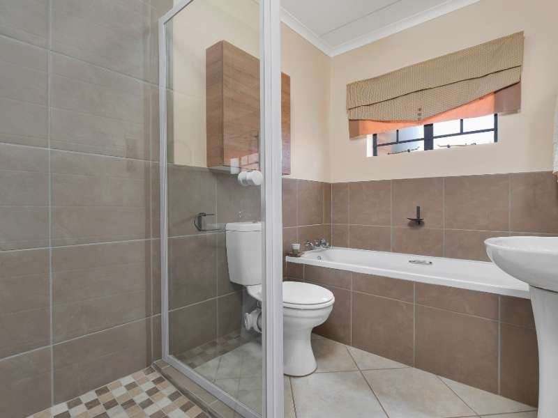 A functional bathroom featuring a shower enclosure, bathtub, pedestal basin, and toilet with neutral wall tiling and a built-in wall cabinet.