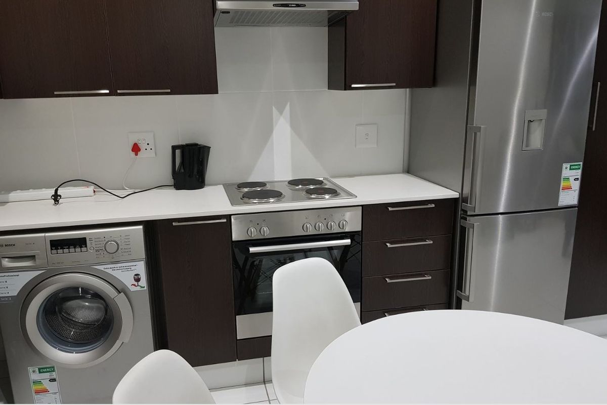 Modern kitchen featuring dark wood cabinetry, white countertops, built-in oven, electric hob, extractor fan, and integrated laundry and refrigeration appliances.