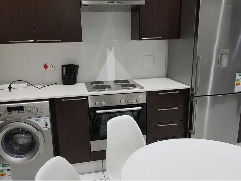 Modern kitchen featuring dark wood cabinetry, white countertops, built-in oven, electric hob, extractor fan, and integrated laundry and refrigeration appliances.