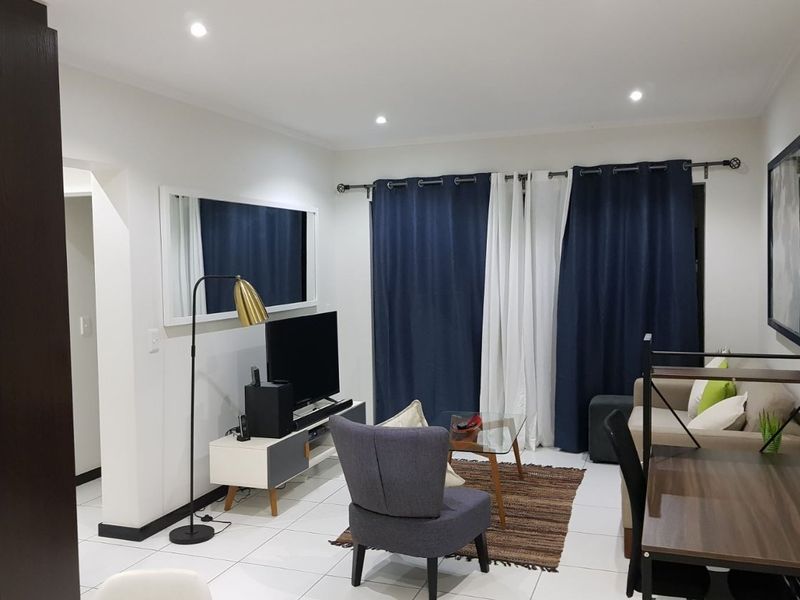A well-maintained living room featuring neutral tiled flooring and recessed downlighting, creating a bright and functional living space.