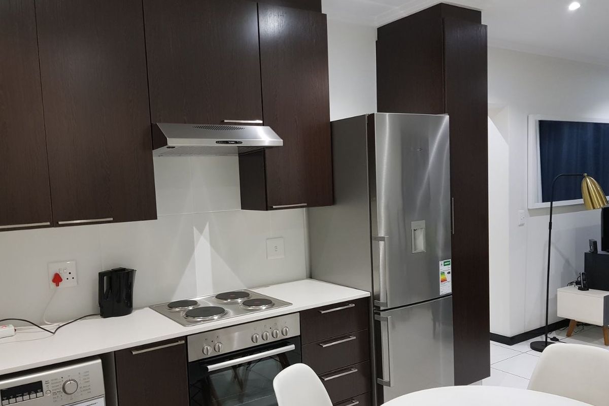 Modern kitchen featuring dark wood cabinetry, white stone countertops, integrated stainless steel appliances, and tiled flooring in an open-plan layout.