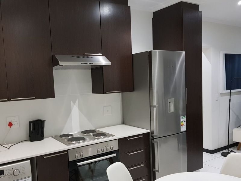 Modern kitchen featuring dark wood cabinetry, white stone countertops, integrated stainless steel appliances, and tiled flooring in an open-plan layout.