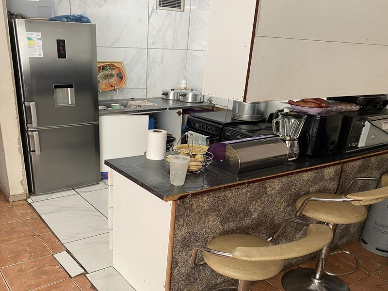 A compact kitchen featuring a breakfast bar, tiled backsplash, and built-in stove. The space shows signs of wear and requires minor cabinetry repairs.
