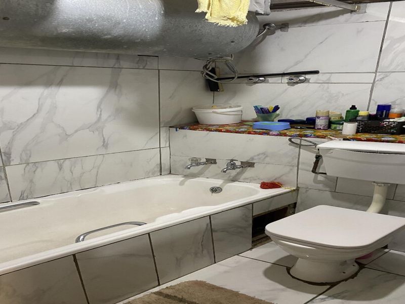 A compact bathroom featuring a bathtub, toilet, and marble-effect wall tiling. The space requires maintenance to address exposed plumbing and missing finishings.