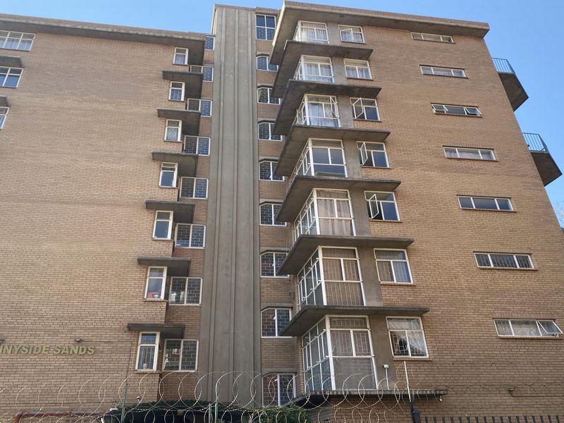 Exterior view of the Sunnyside Sands apartment building, featuring a multi-story brick facade with integrated balconies and perimeter security fencing.