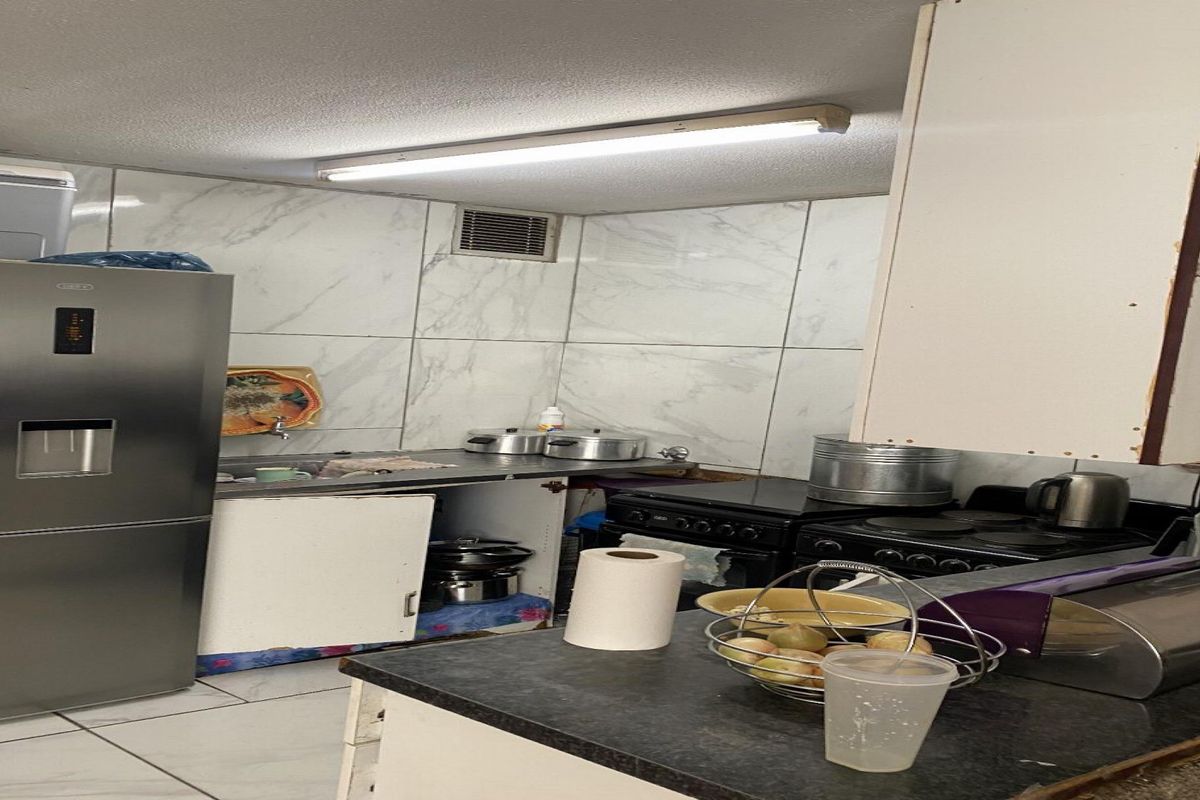 A compact kitchen featuring marble-look wall tiles, built-in cabinetry, and a functional stove and oven setup, requiring some maintenance and cosmetic updates.
