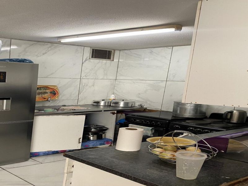 A compact kitchen featuring marble-look wall tiles, built-in cabinetry, and a functional stove and oven setup, requiring some maintenance and cosmetic updates.