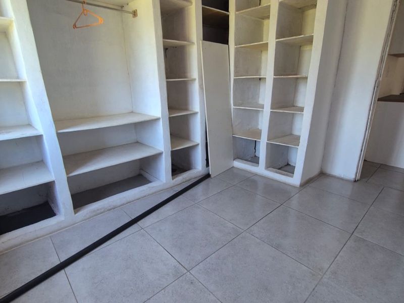 Bedroom featuring built-in shelving and wardrobe units with tiled flooring, requiring cosmetic updates and repairs to the ceiling and cabinetry.