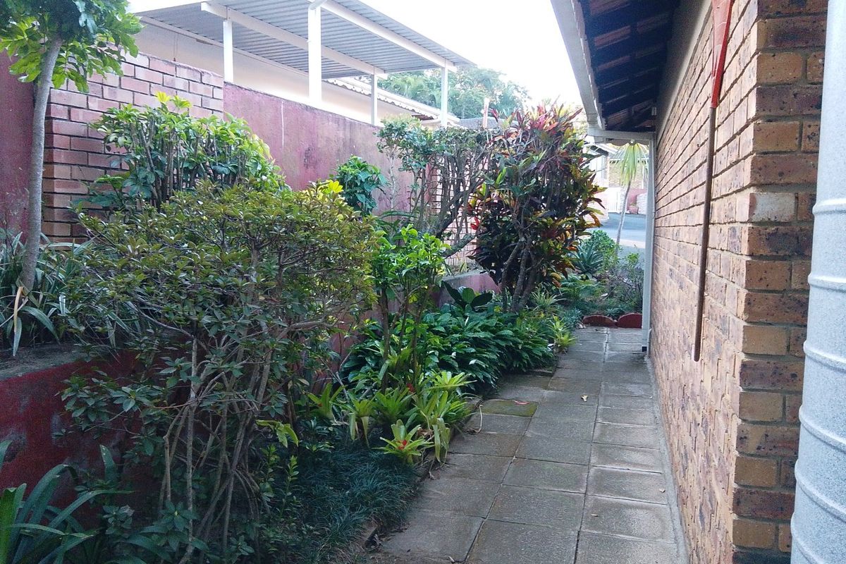 A side garden pathway featuring a paved walkway, established garden beds, and a brick retaining wall along the side of the townhouse.