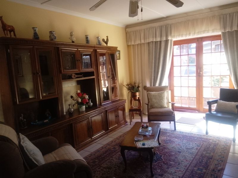 A traditional living room featuring tiled flooring, a ceiling fan, and double french doors providing natural light and access to the exterior.
