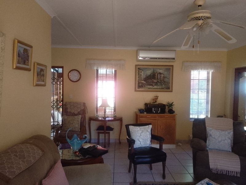 A living room featuring tiled flooring, a ceiling fan, and a wall-mounted split-system air conditioner, with natural light entering through two windows.