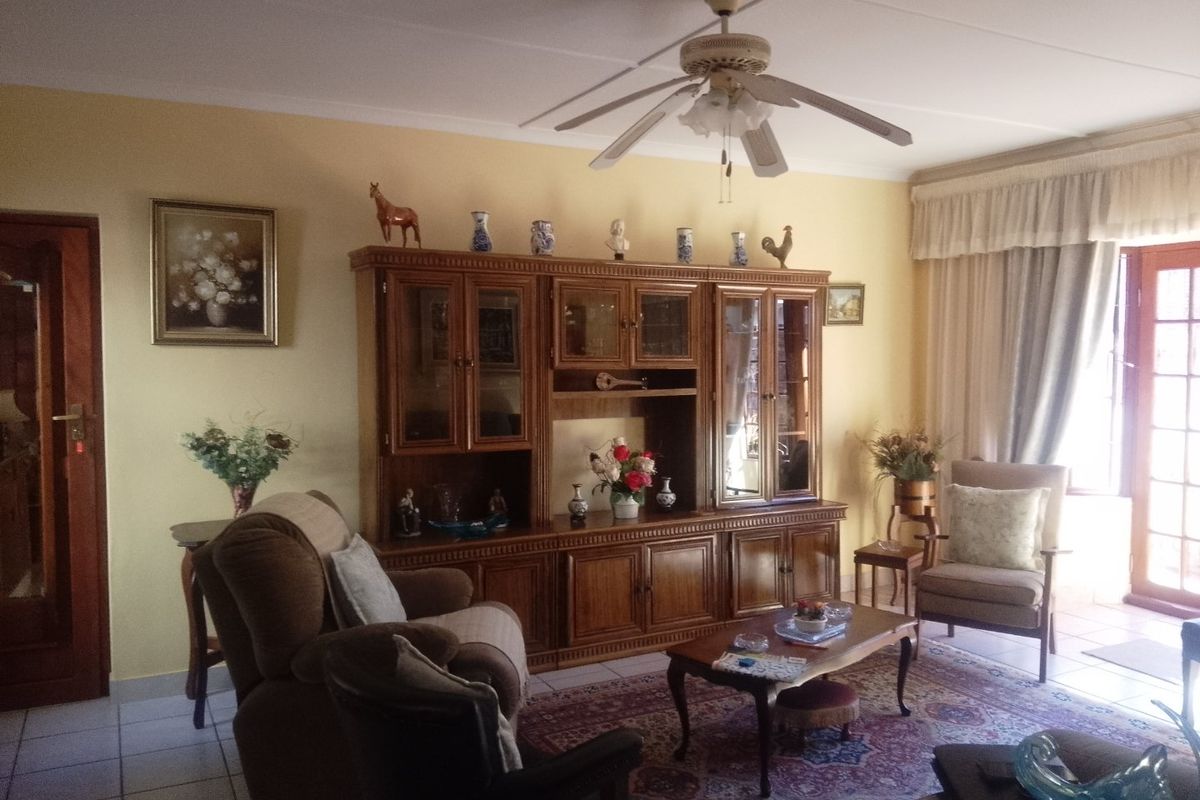 A traditional living room featuring tiled flooring, a ceiling fan, and access to an outdoor area through a timber door.