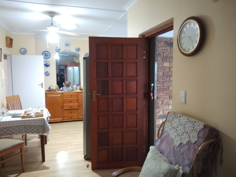 A view of a living area featuring laminate flooring, a ceiling fan, and a timber panel door leading to an adjacent space.
