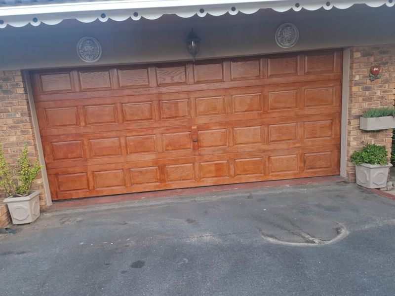 A double garage featuring a polished wooden sectional door set within a brick facade, complemented by an asphalt driveway.