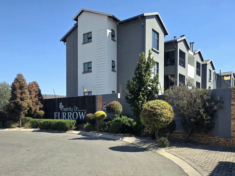 Front exterior view of the Twenty On Furrow townhouse complex, featuring modern multi-story architecture, paved driveway, and established perimeter landscaping.