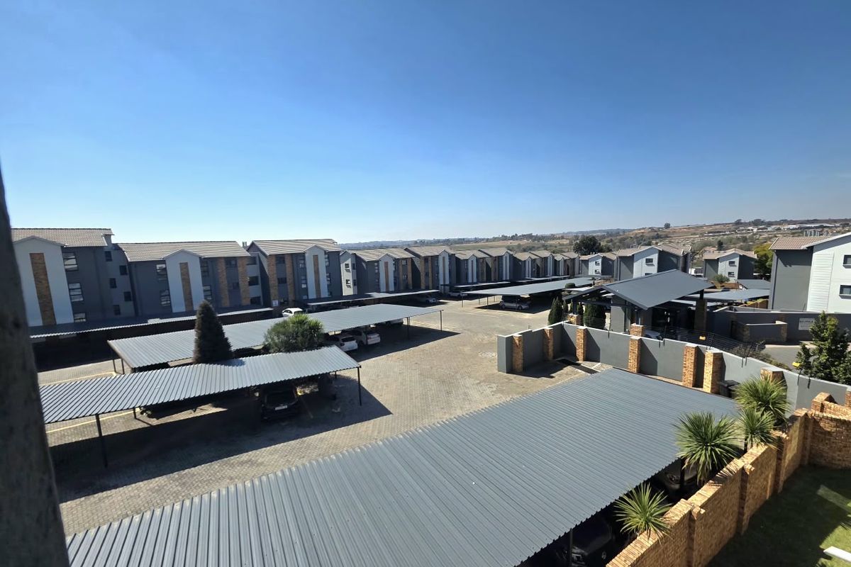 An elevated aerial view of a townhouse complex featuring multiple rows of covered carports, paved driveways, and perimeter brick walling.