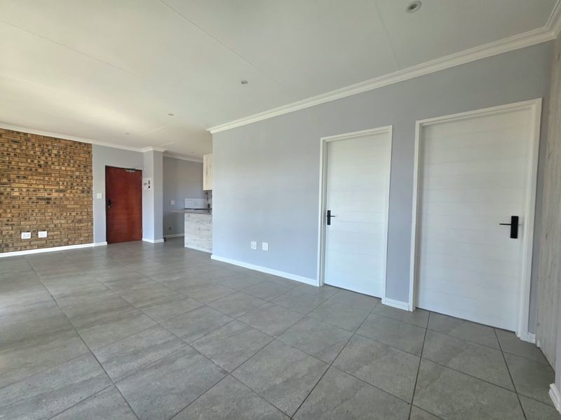 Spacious open-plan living area featuring modern tiled flooring, an exposed brick feature wall, and clean neutral finishes throughout.