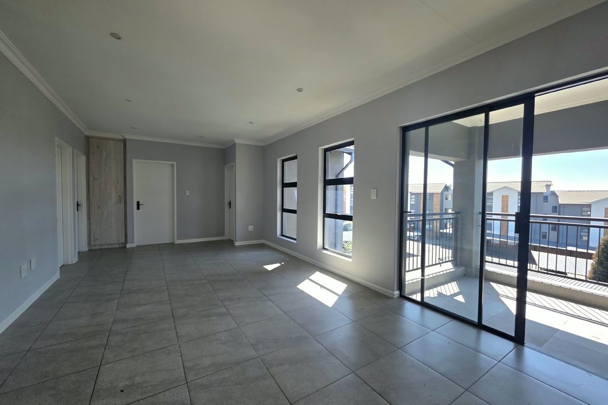 Spacious, light-filled living area featuring neutral tiled flooring, recessed lighting, and large sliding glass doors opening onto a private balcony.