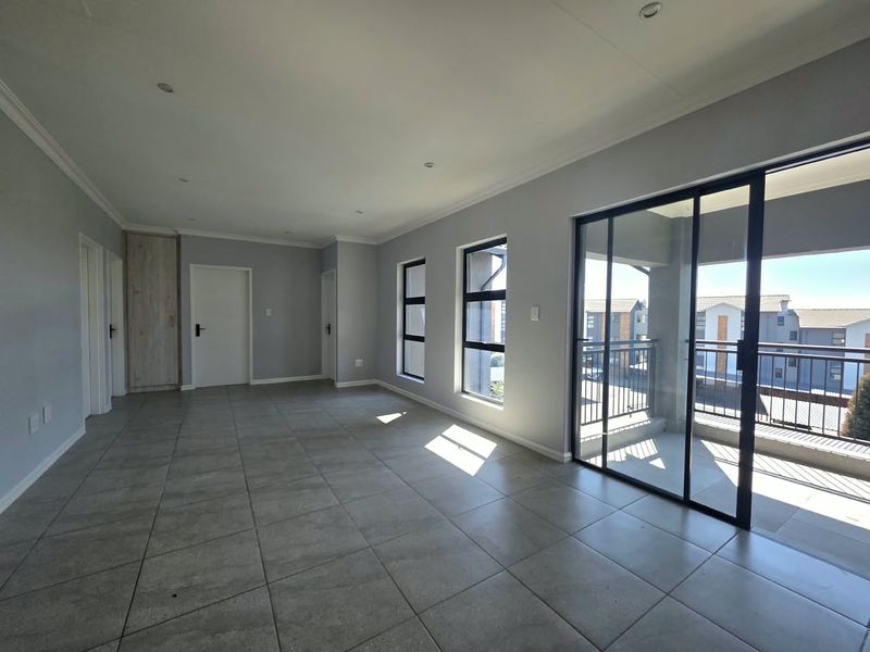 Spacious, light-filled living area featuring neutral tiled flooring, recessed lighting, and large sliding glass doors opening onto a private balcony.