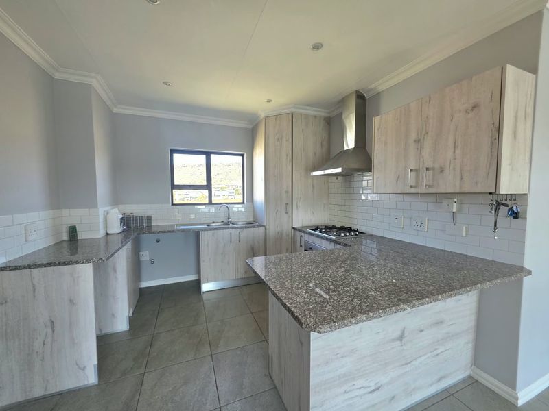 Modern kitchen featuring light wood-grain cabinetry, granite countertops, subway tile backsplash, and a stainless steel extractor fan with a gas hob.