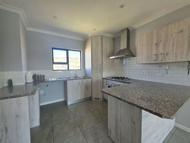 Modern kitchen featuring light wood-grain cabinetry, granite countertops, subway tile backsplash, and integrated stainless steel appliances, including a gas hob and extractor fan.