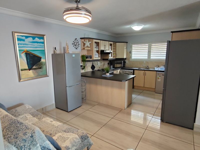 Open-plan kitchen and living area featuring tiled flooring, neutral cabinetry, and integrated lighting, providing a functional and connected living space.