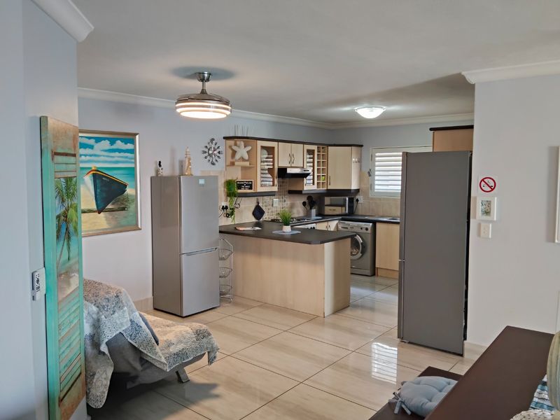 Open-plan kitchen area featuring light-toned cabinetry, tiled flooring, and integrated appliances, seamlessly flowing into the living space.