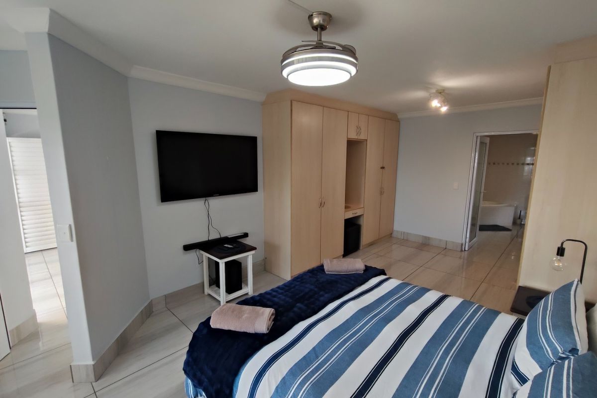 Spacious bedroom featuring neutral tiled flooring, ample built-in cupboard storage, and a ceiling fan, with direct access to an en-suite bathroom.