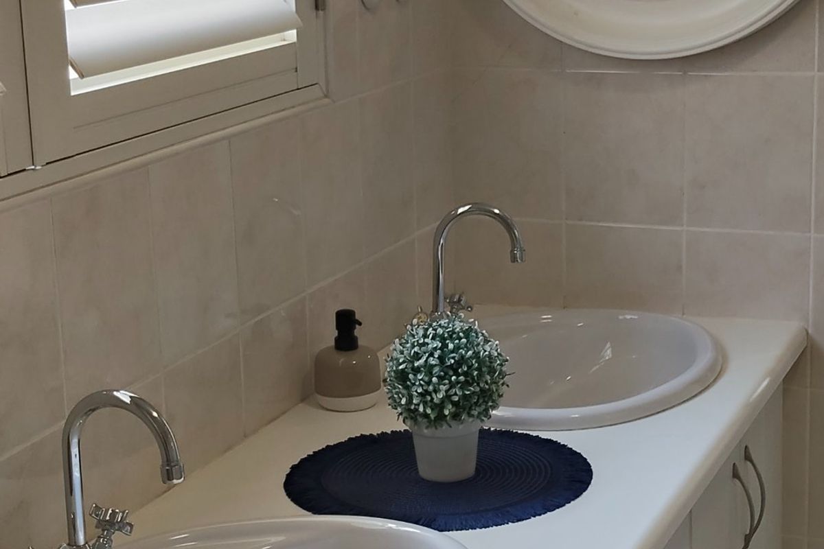 A well-maintained bathroom featuring a double vanity with drop-in sinks, chrome faucets, tiled walls, and shutter blinds.