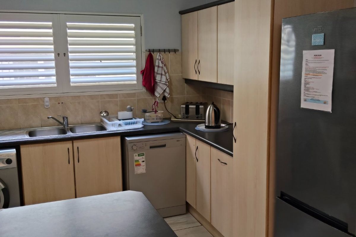 A functional kitchen featuring light wood-tone cabinetry, dark laminate countertops, a double basin sink, and tiled backsplash with integrated appliance spaces.