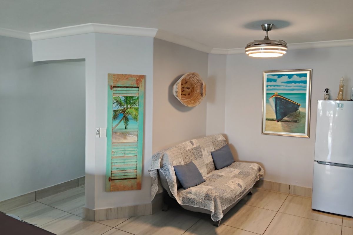 A living area featuring neutral tiled flooring, coved cornicing, and a modern ceiling fan, providing a clean and functional space.