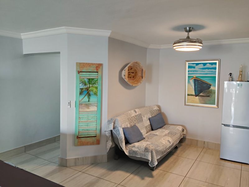 A living area featuring neutral tiled flooring, coved cornicing, and a modern ceiling fan, providing a clean and functional space.