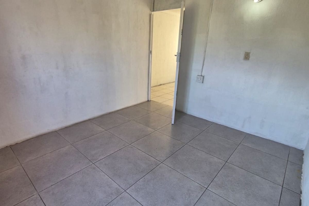 An empty bedroom featuring neutral ceramic floor tiles and basic wall-mounted lighting, presenting a blank canvas for potential interior design updates.