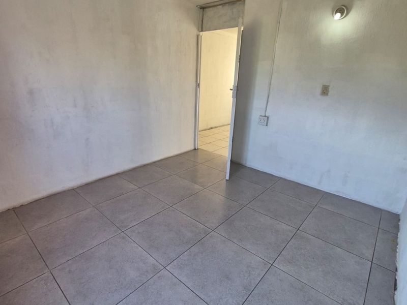 An empty bedroom featuring neutral ceramic floor tiles and basic wall-mounted lighting, presenting a blank canvas for potential interior design updates.