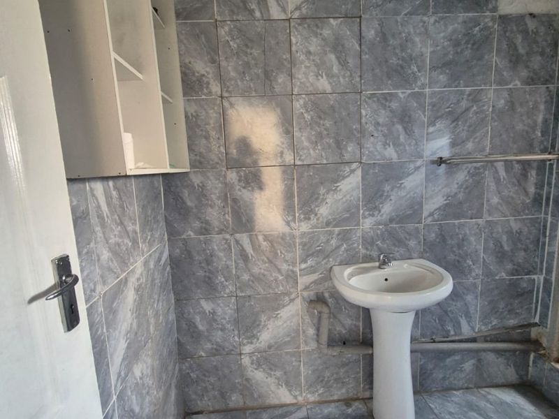 A small bathroom featuring grey marble-effect wall and floor tiles, a pedestal washbasin, and built-in shelving, currently requiring cosmetic updates and finishing.