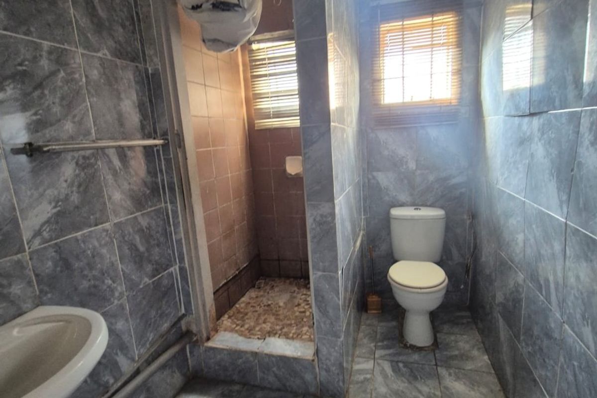 A dated bathroom featuring grey marble-effect wall and floor tiles, a pedestal basin, a separate shower enclosure, and a standard toilet.