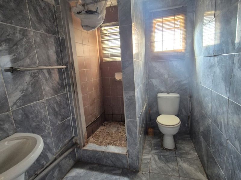 A dated bathroom featuring grey marble-effect wall and floor tiles, a pedestal basin, a separate shower enclosure, and a standard toilet.