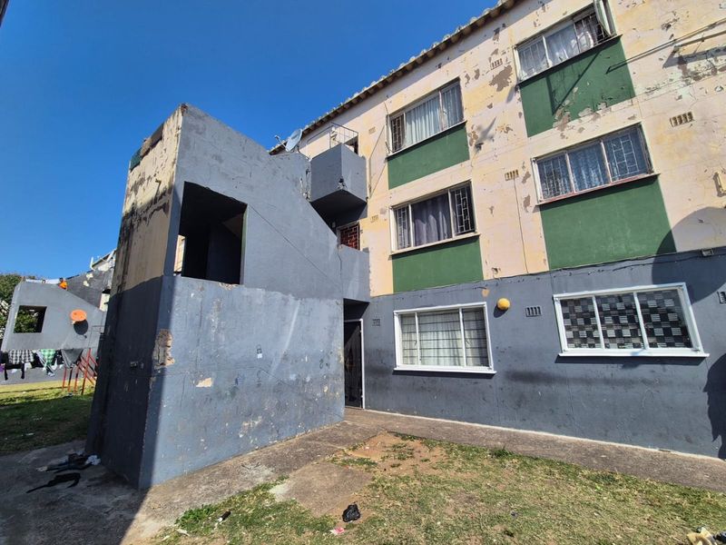 Rear view of an apartment building showing significant exterior wear, peeling paint, and exposed concrete surfaces requiring maintenance.