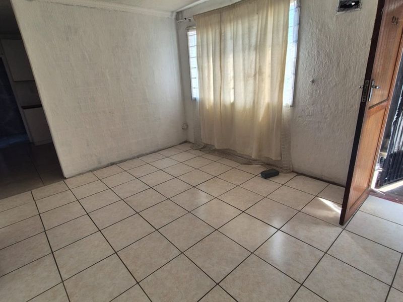 An empty living room featuring tiled flooring and a window, providing a blank canvas for potential interior design updates.