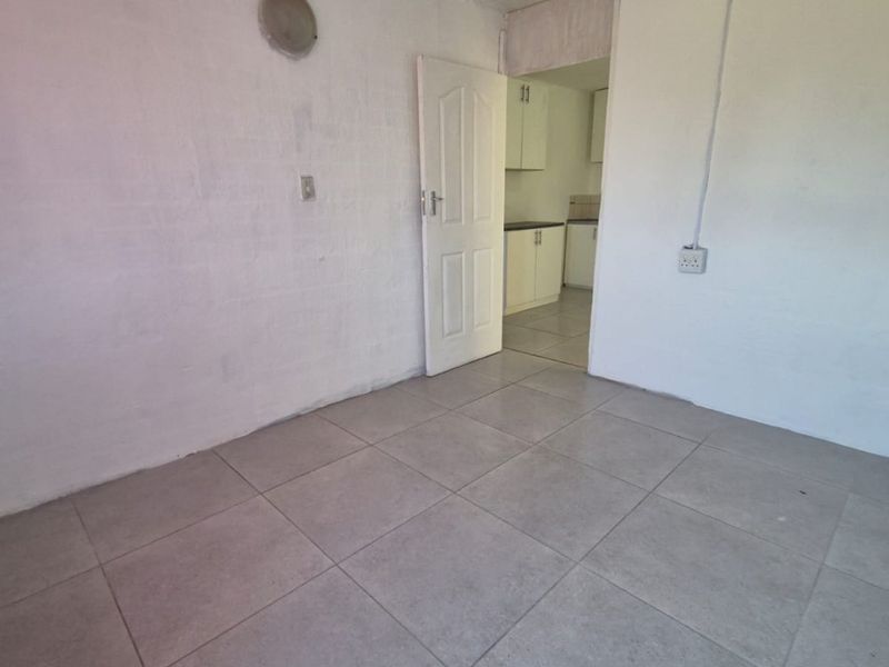 An empty living area featuring tiled flooring and direct access to the kitchen, presenting a blank canvas for renovation and interior design.