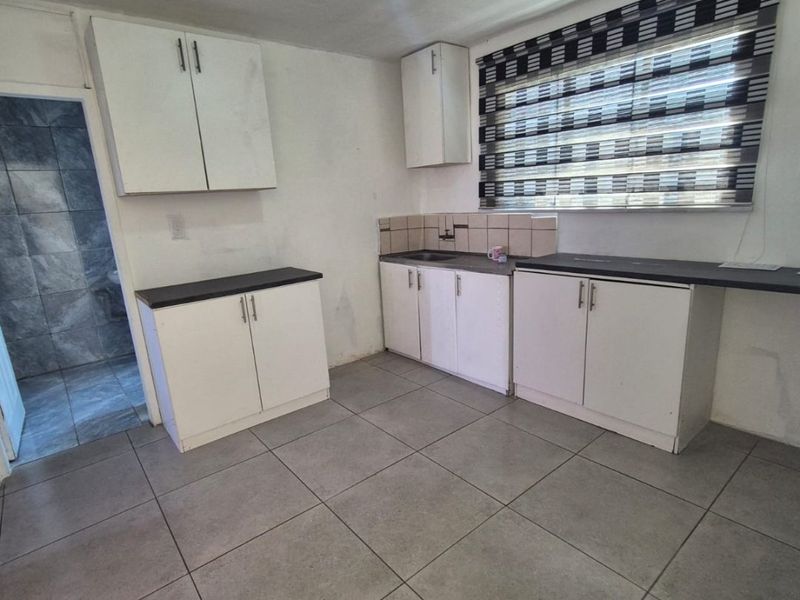 A functional kitchen featuring white built-in cabinetry, dark laminate countertops, tiled flooring, and a window with roller blinds.