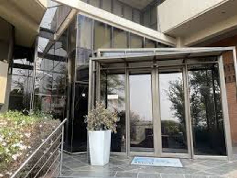 Modern commercial building entrance featuring a glass facade, aluminium framing, and stone tile flooring under a covered canopy.