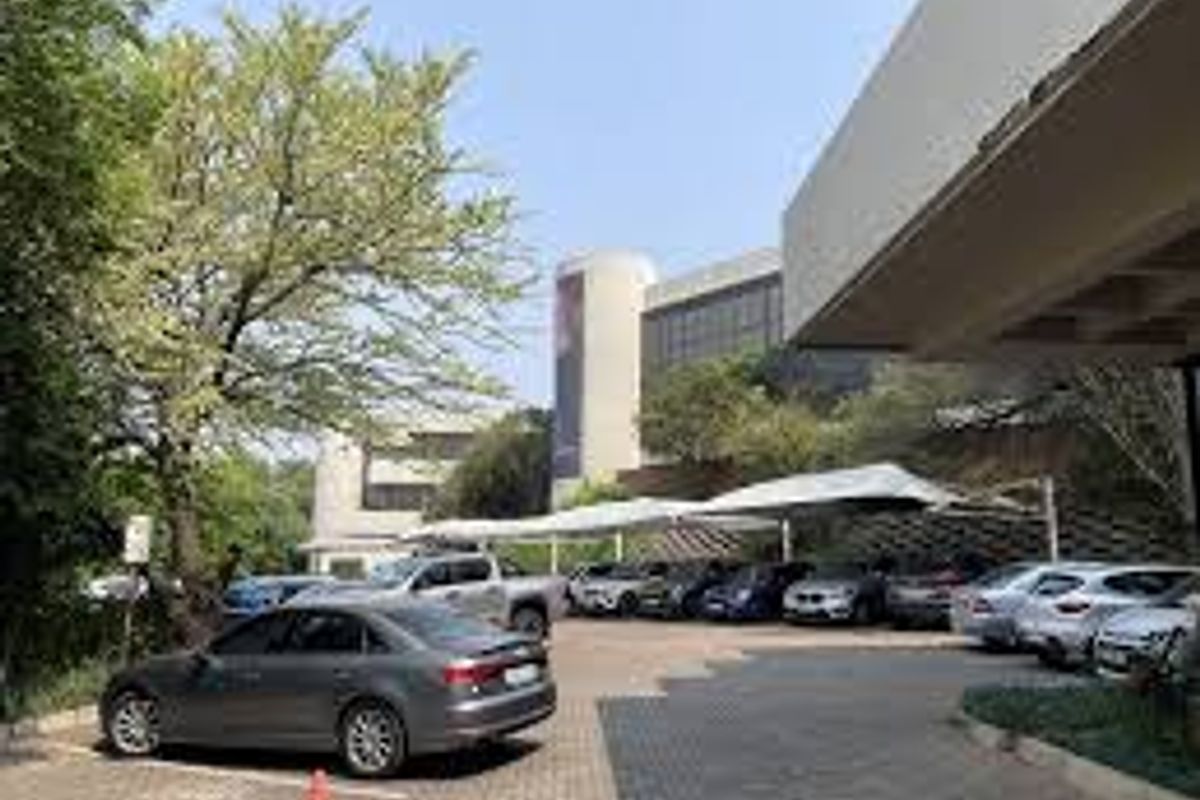Exterior view of a commercial property featuring a paved parking area with shade cloth carports and modern concrete building architecture.