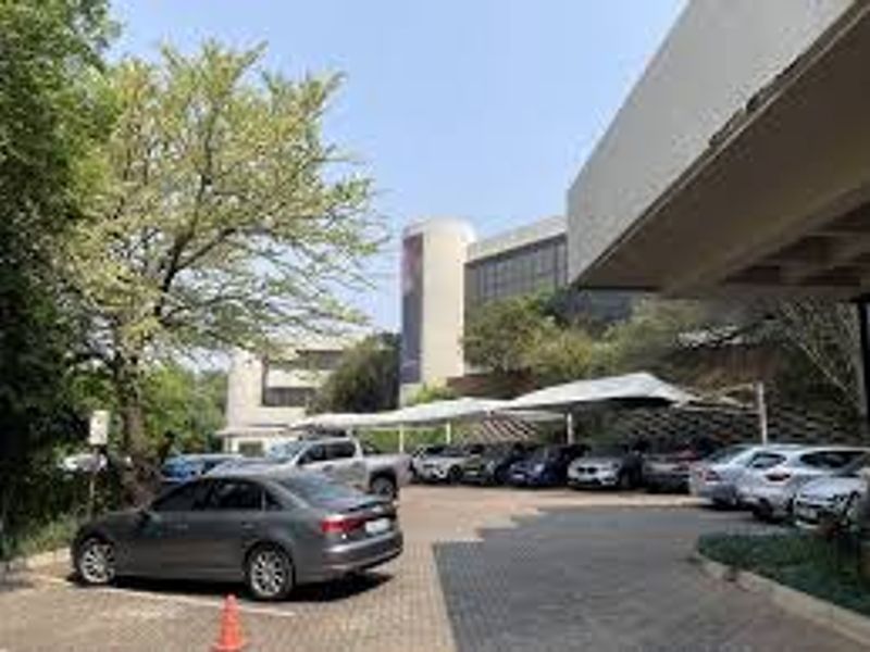 Exterior view of a commercial property featuring a paved parking area with shade cloth carports and modern concrete building architecture.