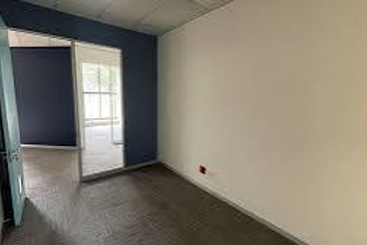 A vacant commercial office space featuring carpeted flooring, a suspended ceiling, and a glass partition wall leading to an adjacent office area.