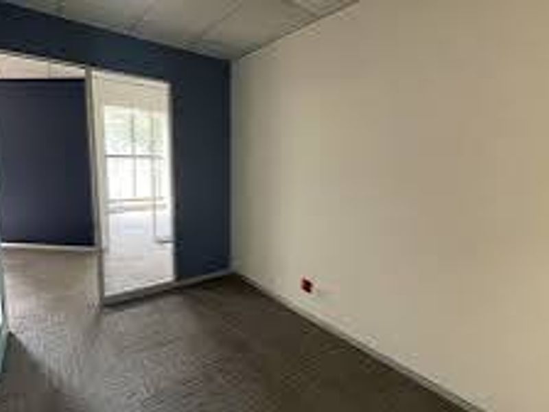 A vacant commercial office space featuring carpeted flooring, a suspended ceiling, and a glass partition wall leading to an adjacent office area.