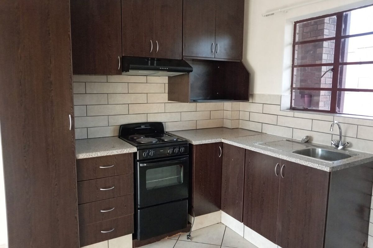 A functional kitchen featuring dark wood cabinetry, subway tile backsplash, laminate countertops, and a freestanding electric stove with an extractor fan.