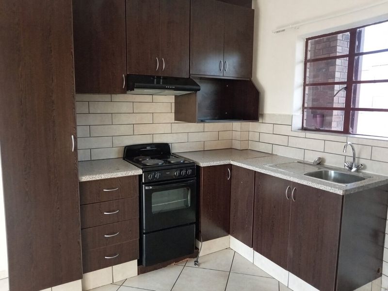 A functional kitchen featuring dark wood cabinetry, subway tile backsplash, laminate countertops, and a freestanding electric stove with an extractor fan.