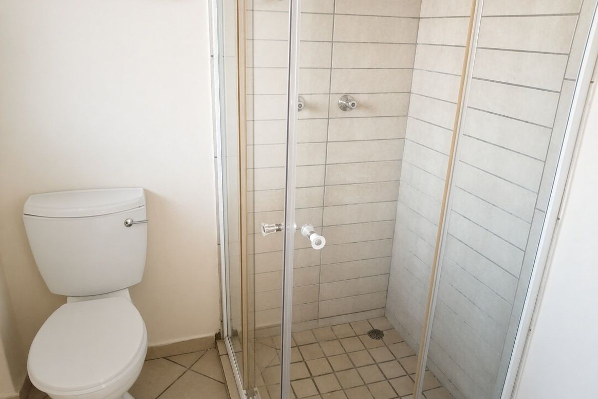 A functional bathroom featuring a white toilet and a glass-enclosed shower with neutral wall and floor tiling.